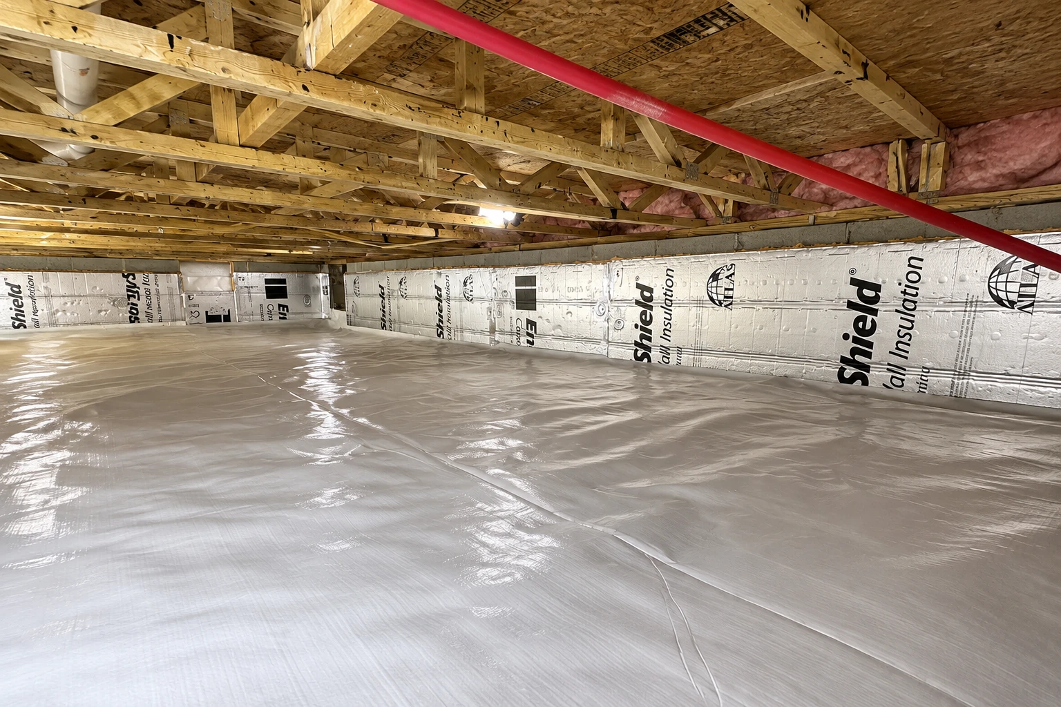 A crawl space has a reflective plastic vapor barrier across the floor and insulated panels along the low walls.