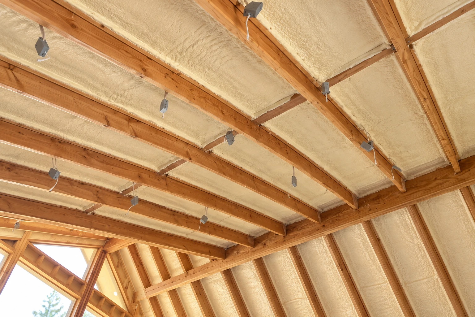 Open-cell foam insulation fills the ceiling bays of a timber-framed structure, with electrical boxes and wiring visible.