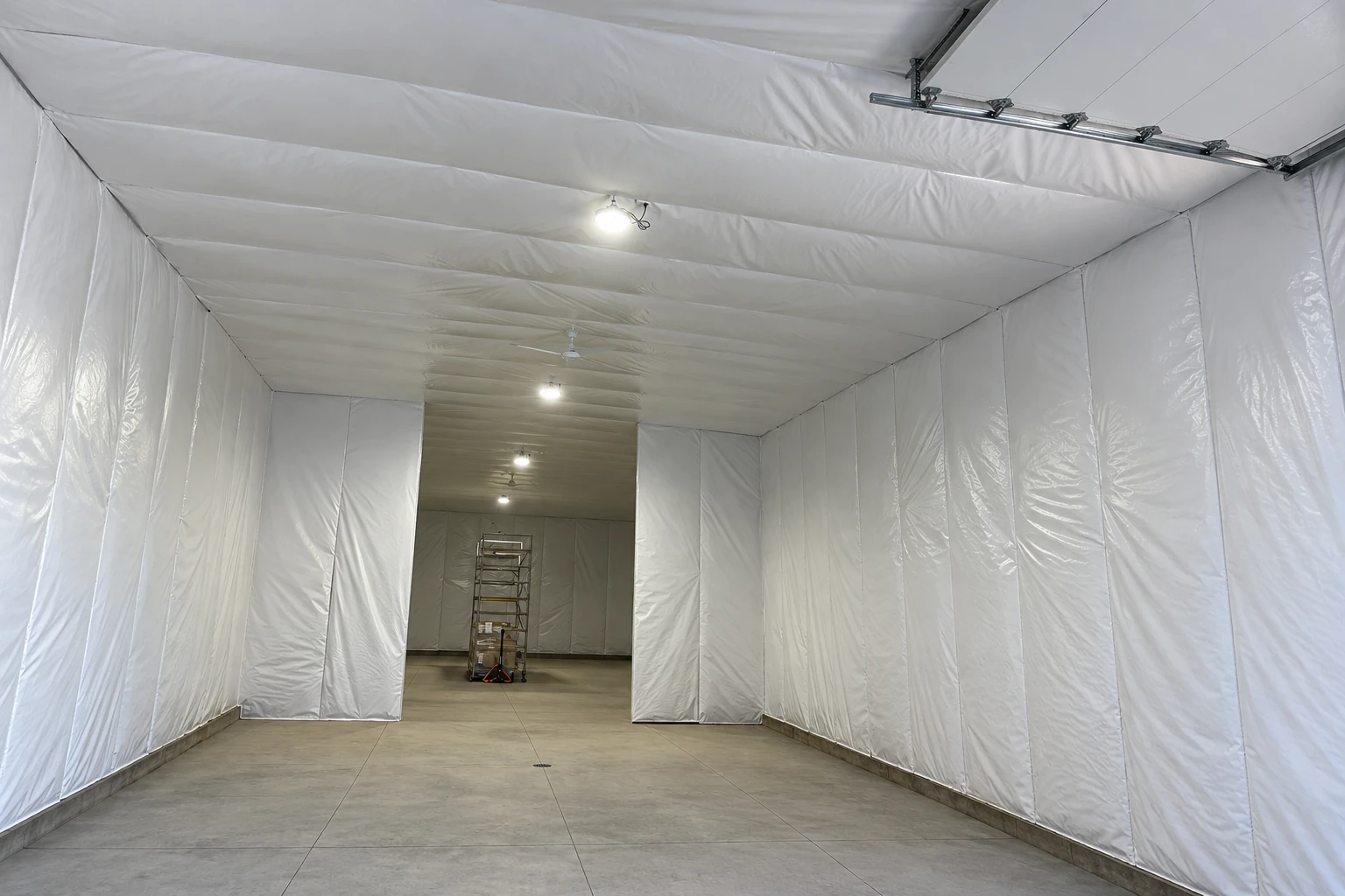 A long interior is lined with white vapor barrier sheeting on the walls and ceiling, with lights and a concrete floor.
